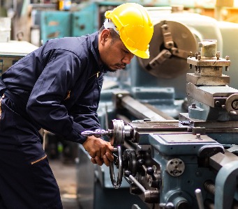 Factory Asian male worker. Asian man Lathe worker in production plant drilling at machine on the factory. Yellow hard hat safety first at mechanic factory.